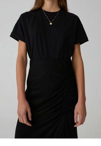T-shirt nera con maniche corte arrotolate abbinata a una gonna nera arricciata. Tessuto liscio con una vestibilità comoda e un sottile dettaglio di arricciatura.