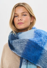 Blå ternet tørklæde lavet af blødt uld, med forskellige nuancer af blå i et stort, hyggeligt design. Glat tekstur med et varmt udseende.