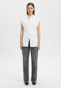 Vit ärmlös blus med en traditionell krage och knäppning fram, i kombination med högmidjade grå denimjeans och spetsiga svarta klackar.