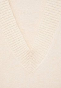 Pullover de culoare crem, cu un decolteu în V, având detalii texturate sub formă de creneluri în jurul gulerului, fabricat dintr-un material moale, tricotat.