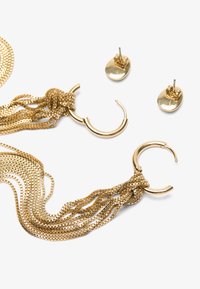 Gold-tone metal earrings featuring long chain strands and a circular hoop design, with smooth oval studs included. Textured and shiny finish.
