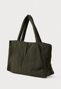 Μεγάλη σκούρα πράσινη μαλακή τσάντα tote με δύο μαλακούς χειρολαβές, που στέκεται όρθια σε μια απλή ανοιχτόχρωμη φόντο.