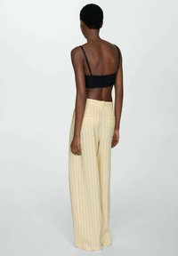 Black cropped bralette with thin straps paired with high-waisted yellow striped wide-leg trousers. Soft fabric, vertical stripes, and pockets.