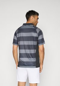 Grijs en zwart gestreept sportshirt met een kraag, korte mouwen en contrasterende zijpanelen, gecombineerd met witte shorts.