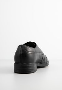 Scarpa in pelle nera con tacco basso, texture liscia, forma arrotondata e dettagli di cucitura lungo i lati. Adatta per abbigliamento formale o informale.
