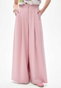 Lichtroze wijde broek met hoge taille, voorzien van twee zakken aan de voorkant en een dubbele knoopsluiting in de taille. Gladde stofstructuur.