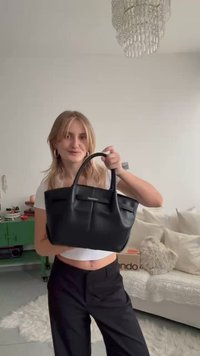 Black leather handbag with a structured design, prominent top handles, and embossed logo. Smooth texture and minimalist accents.