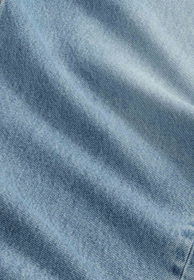 Tissu en denim bleu clair avec une texture en sergé diagonal et des plis doux créant des ombres et des reflets.