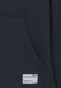 Sudadera azul marino con una tela suave y texturizada. Presenta un bolsillo delantero y una etiqueta blanca con instrucciones de cuidado y marca.