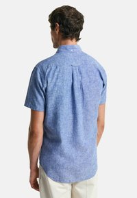 Kortmouwige blauwe chambray shirt met een rugpand en plooi. Glad textuur, casual fit, afgeronde zoom en een knoopsluiting bij de kraag.