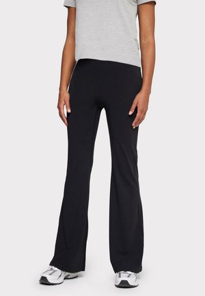 Pantalons évasés noirs en tissu extensible, avec une texture lisse et une taille ajustée, associés à un tee-shirt gris à manches courtes.