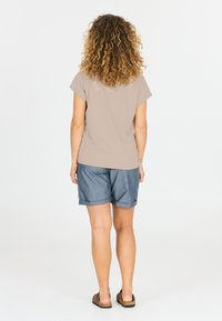 Beige T-shirt met korte mouwen, gecombineerd met denim short. De short is omgeslagen aan de zoom, heeft een losse pasvorm en een lichte textuur. Platte sandalen worden gedragen.