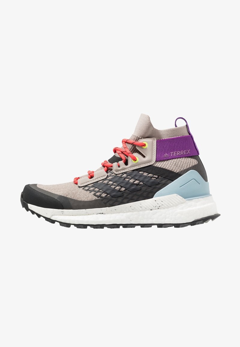 Chaussure de randonnée montante Adidas Terrex en maille beige avec accents noirs, lacets corail vif, bride de talon violette et semelle blanche rembourrée.