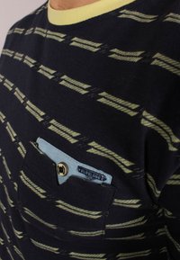 Navy lyhythihainen paita keltaisilla yksityiskohdilla, jossa on raidallinen kuosi ja vaaleansininen tasku napin yksityiskohdalla.