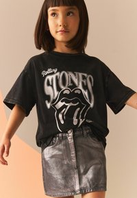 Sort oversized t-shirt med Rolling Stones grafik; skinnende sølv denim nederdel med lommer og frontlukning med knapper.