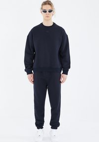 Navy Sweatshirt- und Jogginghose-Set, aus einem Baumwollmischgewebe hergestellt. Verfügt über einen gerippten Halsausschnitt, Bündchen und Knöchelbündchen, mit einem dezenten Logo-Detail.