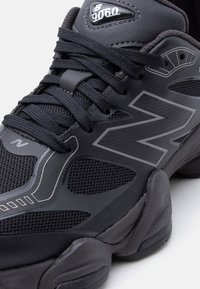 Pantof sport New Balance 9060 negru cu partea superioară din plasă și material sintetic, logo-ul proeminent "N" pe lateral și talpă groasă texturată.