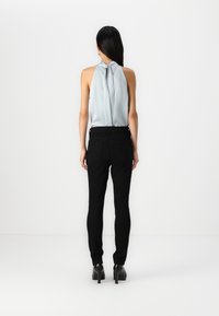 Ljusblå ärmlös topp med ett knyt baktill, matchad med svarta slim-fit byxor och svarta klackar, sedd bakifrån.