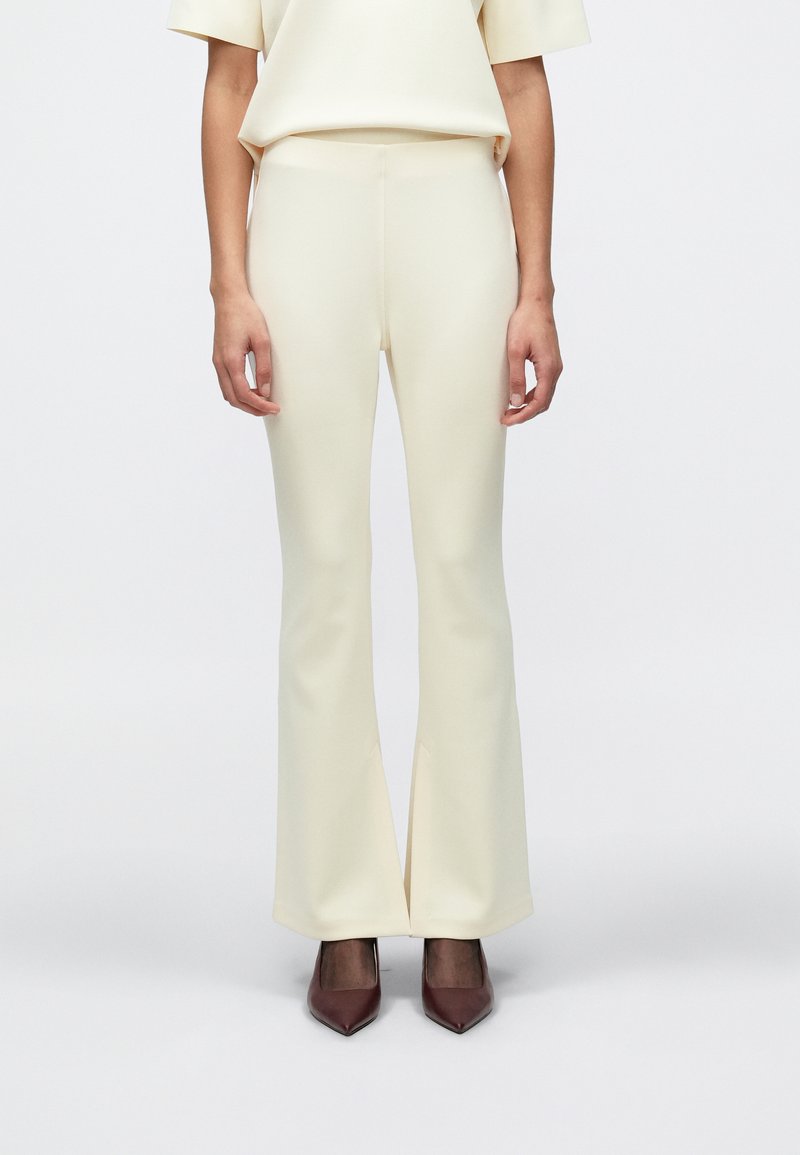 Εκρού παντελόνια με φαρδιά γραμμή, λεία υφή και ραμμένη εφαρμογή, με μέτριο ύψος μέσης και διακριτικές σκισίματα μπροστά στους αστραγάλους.