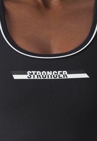 Svart sports tank topp med hvite detaljer, med ordet "STRONGER" i fet skrift. Laget av jevnt, elastisk materiale.