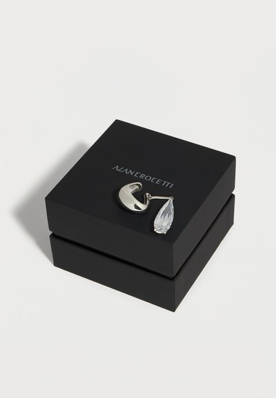 Ασημένιο σκουλαρίκι σε σχήμα ημισελήνου με διαφανή πολύτιμη πέτρα σε σχήμα σταγόνας, τοποθετημένο σε μαύρο κουτί κοσμημάτων NAN CROVETTI.