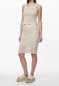Conjunto de dos piezas de color beige, tejido, que consiste en un top sin mangas con tirantes anchos y una falda hasta la rodilla, con un patrón de tejido texturizado y abierto.