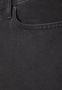 Tejido de mezclilla negra con una textura suave, contornos de bolsillo estándar y detalles de costura discretos, mostrando un diseño clásico de jeans.