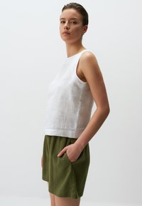 Top senza maniche in lino bianco con scollo rotondo, abbinato a pantaloni corti verde oliva con tasche laterali. Tessuto liscio e vestibilità comoda.