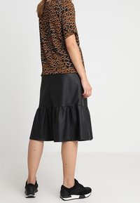 Top marrón de manga corta con un patrón de manchas, combinado con una falda negra de imitación piel con volantes, usada con zapatillas deportivas negras.