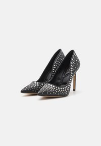 Des chaussures à talons hauts noires avec des pointes acérées, ornées d'éclats en argent sur le dessus, présentant un design élégant et une finition en cuir texturé.