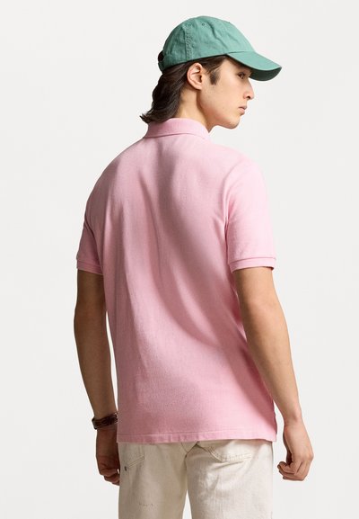 Polo de manga corta en algodón de color rosa claro con un cuello clásico. Combinado con una gorra verde, mostrado desde atrás. Diseño casual.