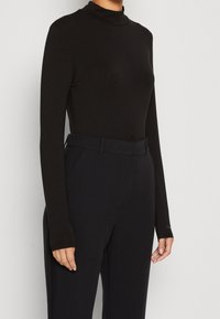 Schwarzes Turtleneck-Shirt mit langen Ärmeln aus glattem Stoff, taillierte Passform, kombiniert mit hochgeschnittenen schwarzen Hosen und einem passenden Gürtel.