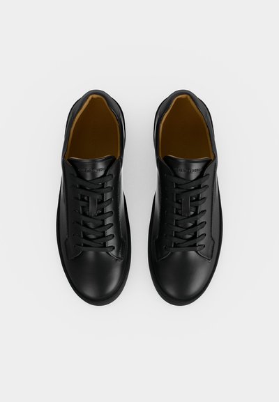 Ζευγάρι μαύρα δερμάτινα sneakers με κορδόνια και καφέ εσωτερική επένδυση, βλέποντας από πάνω σε λευκό φόντο.