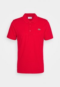 Red polo shirt made of cotton with a collar, three button placket, short sleeves, and a small green crocodile logo on the left chest.