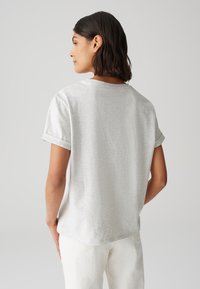 T-shirt gris clair à manches courtes avec une coupe décontractée, poignets retroussés et texture douce, vu de dos avec un ourlet légèrement arrondi.