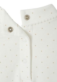 White fabric with gold polka dots; features metal snaps at the collar and decorative scalloped trim. Soft cotton texture.