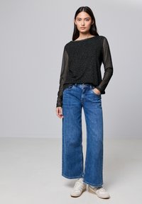 Top long à manches noires avec imprimé léopard en tissu transparent, associé à un jean bleu taille haute à jambes larges et des baskets blanches.