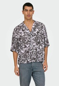 Camisa de manga corta, de corte holgado, en estampado de leopardo gris y negro sobre fondo blanco, con cuello con muescas y cierre de botones.