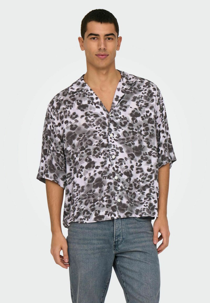 Camisa de manga corta, de corte holgado, en estampado de leopardo gris y negro sobre fondo blanco, con cuello con muescas y cierre de botones.