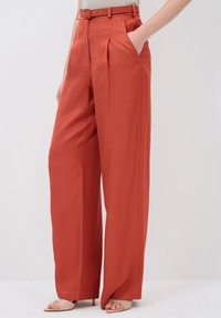 Wide-legged trousers in a vibrant rust color, featuring a belted waist, pleats, and side pockets. Smooth fabric with a tailored silhouette.