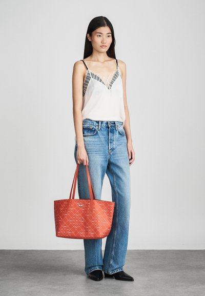 Borsa a tracolla rossa con motivo, dotata di doppi manici, abbinata a una maglietta chiara con scollatura a V e dettagli in pizzo, indossata con jeans a gamba dritta di un blu chiaro.
