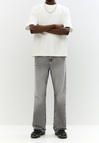 Weißes T-Shirt mit kurzen Ärmeln, lockere Passform. Graue Denim-Jeans mit verwaschenem Finish. Schwarze Sneaker mit strukturierten Details. Einfacher silberner Halskette.