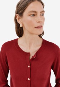Cardigan rosso scuro realizzato in morbido materiale, con scollatura tonda, bottoni dorati e una vestibilità slim. Maniche e orlo a coste ben evidenti.