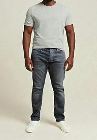 Šedé tričko s krátkým rukávem, tmavé džínové kalhoty, doplněné bílými teniskami, s uvolněným střihem a jemným vyblednutím džínoviny.