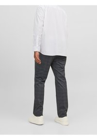 Szare spodnie w kratę wykonane z tkaniny o gładkiej fakturze, zestawione z białą koszulą zapinaną na guziki i białymi trampkami.