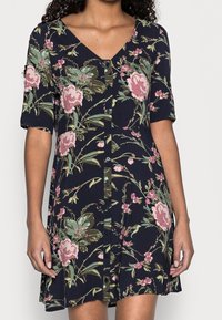 Abito floreale al ginocchio in tessuto blu navy, con maniche corte, scollatura a V e dettagli con bottoni lungo la parte anteriore. Accentuato da fiori rosa e verdi.
