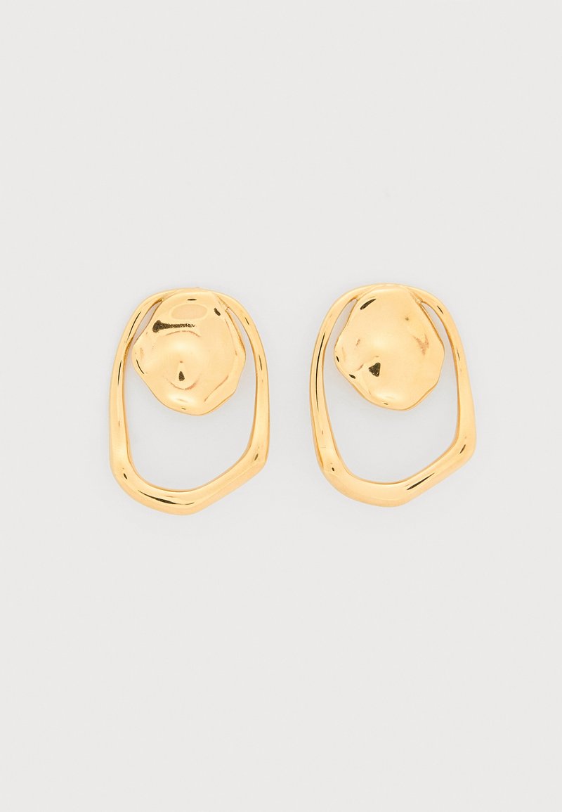 Σκουλαρίκια καρφάκια από χρυσό τόνο με ακανόνιστο οβάλ σχήμα, με υφή στο συμπαγές κέντρο και ανοιχτό λείο περίγραμμα σε λευκό φόντο.