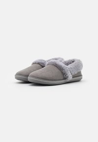 Grijze sloffen gemaakt van zachte suède met een fuzzy grijze voering, voorzien van een ronde neus en platte zool met decoratieve stiksels langs de rand.
