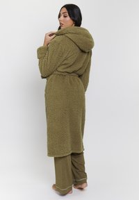 Olivgrön huva klänning gjord av plysch, texturerat tyg, med ett knytbälte, som bärs över matchande löst sittande olivbyxor med vit kant.