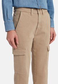 Beige katoenen cargobroek met twee zijzakken, rechte pasvorm en subtiele textuur, gedragen met een lichtblauw denimshirt.